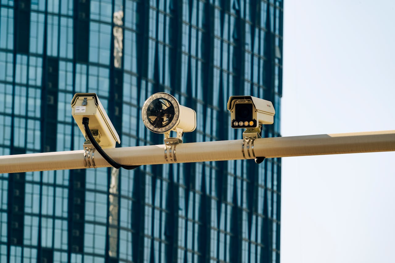 heros-img Surveillance cameras mounted on a pole in front of a modern glass building.