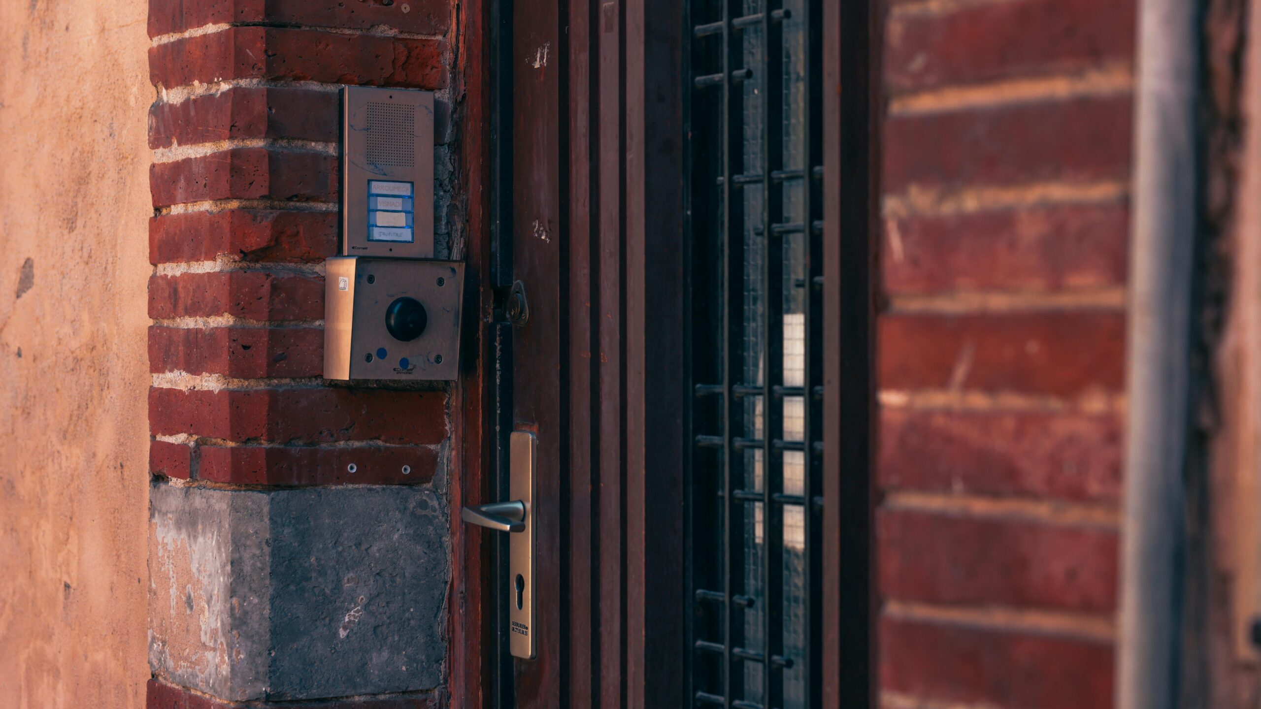 Close-up of a brick wall with a security intercom and door handles in Toulouse, France.